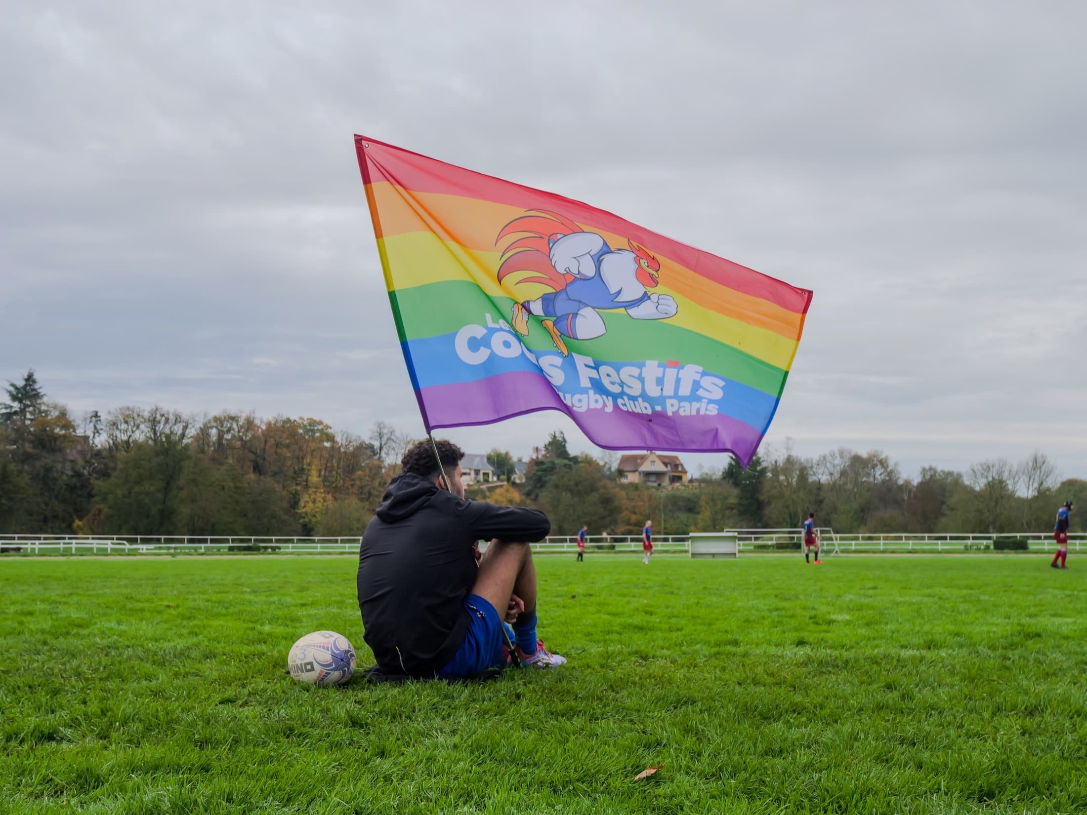 Joueur des Coqs Festifs avec drapeau et ballon au bord du terrain